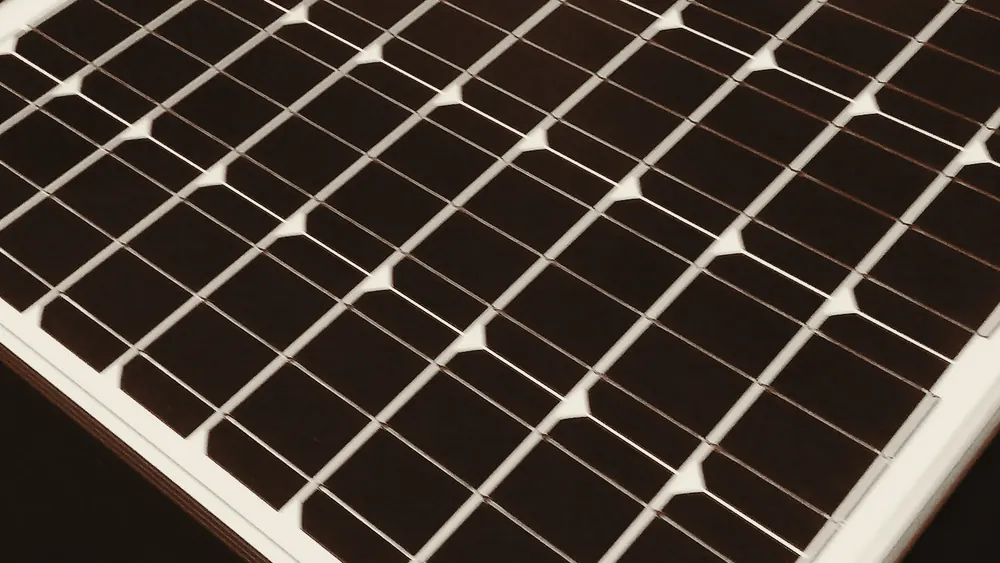 Close view across the cell grid of a monocrystalline solar panel, showing the square cells and the thin silver busbars between them.